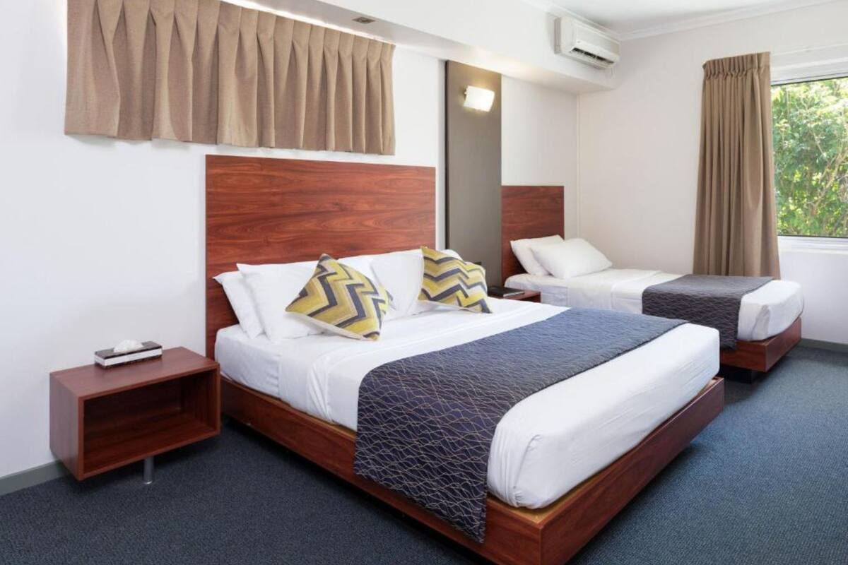 A hotel room with a large bed, a smaller bed, a nightstand, and a window with curtains.