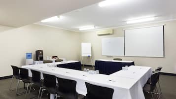 A conference room with a long table, chairs, a whiteboard, and a projector screen.