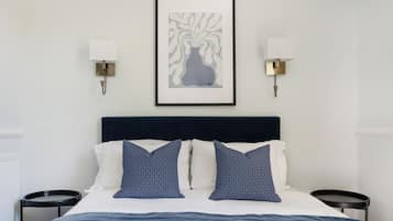 A hotel room with a bed, two bedside tables, a framed artwork on the wall, and two wall-mounted lamps.