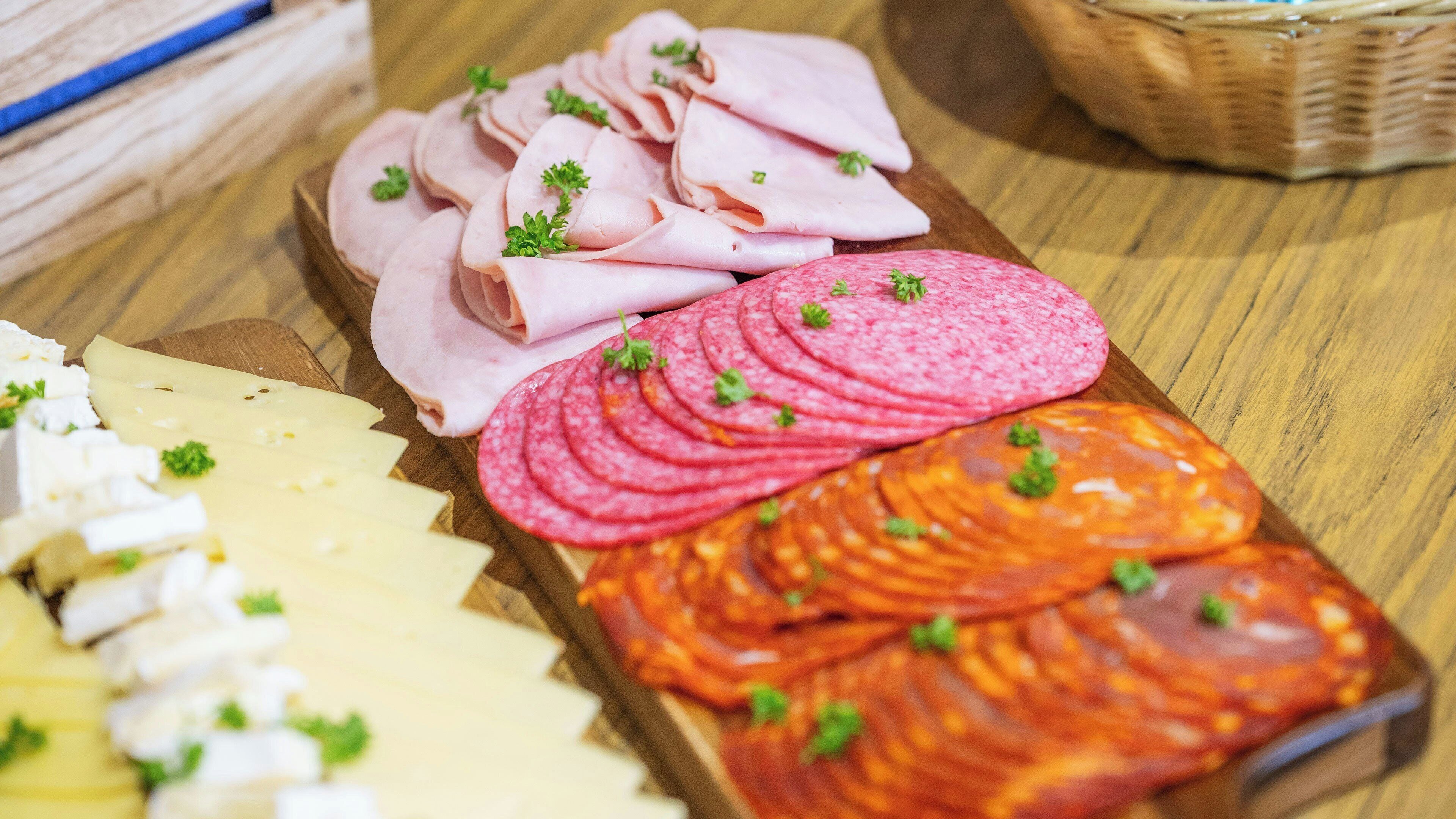 En träbricka med olika sorters mat, inklusive skivad kött och ost.