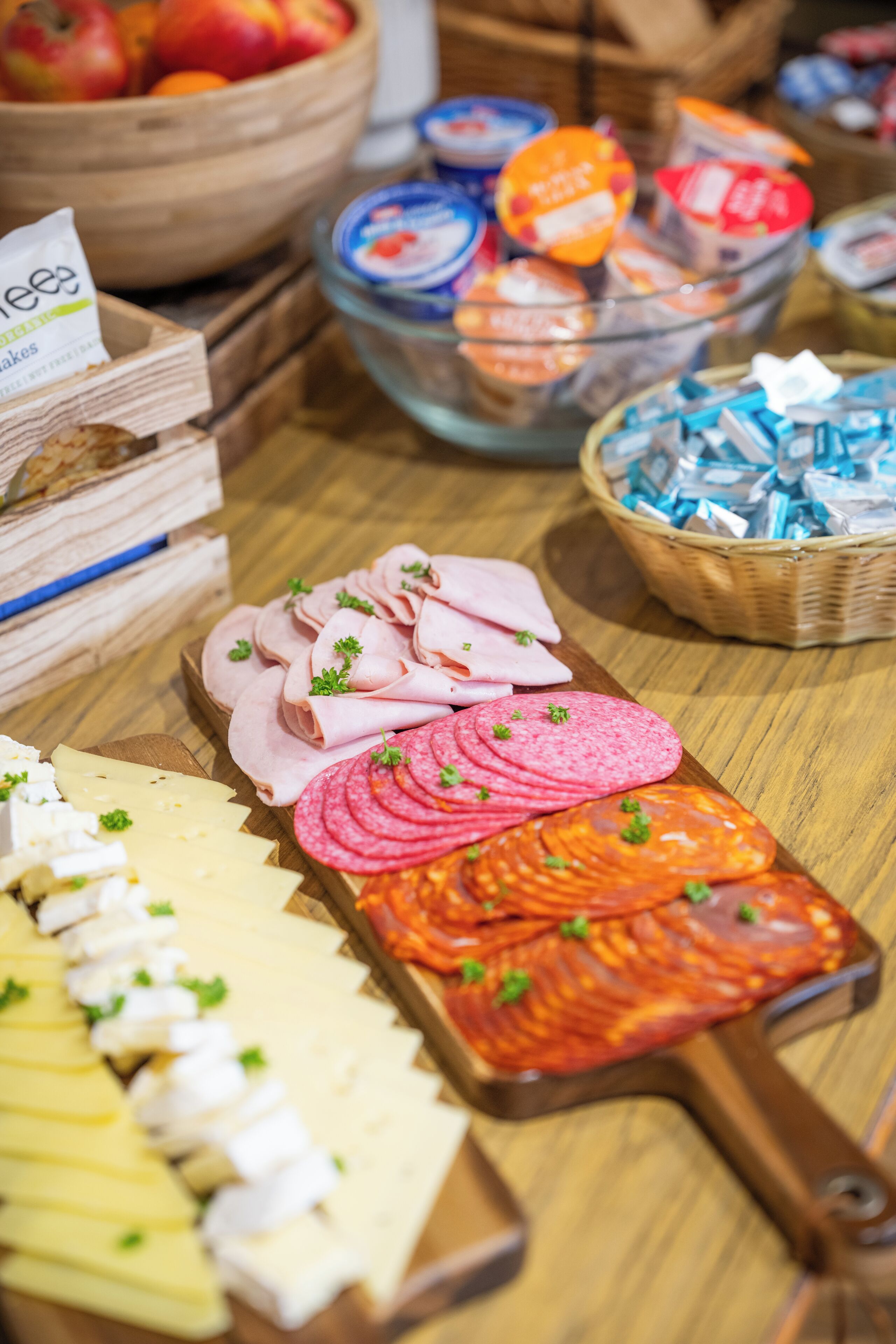 A variety of food items including sliced meats, cheeses, and packaged goods on a wooden table.