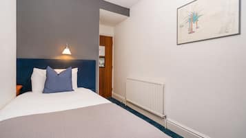 A hotel room with a large bed, a headboard, a wall-mounted light, a radiator, and a framed picture on the wall.
