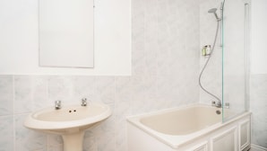 Un baño con lavamanos pedestal, bañera y ducha con puerta de cristal.