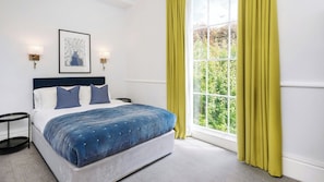 Un dormitorio con una cama, dos lámparas de pared, una ventana con cortinas y una obra enmarcada en la pared.