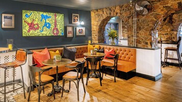 Un rincón de bar acogedor con una pared de piedra, una disposición de asientos con sillones y un sofá, y obras de arte en las paredes.