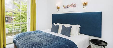 Hotellihuone, jossa on suuri sänky, ikkuna, jossa on verhot, ja kaksi seinälle asennettua valaisinta.