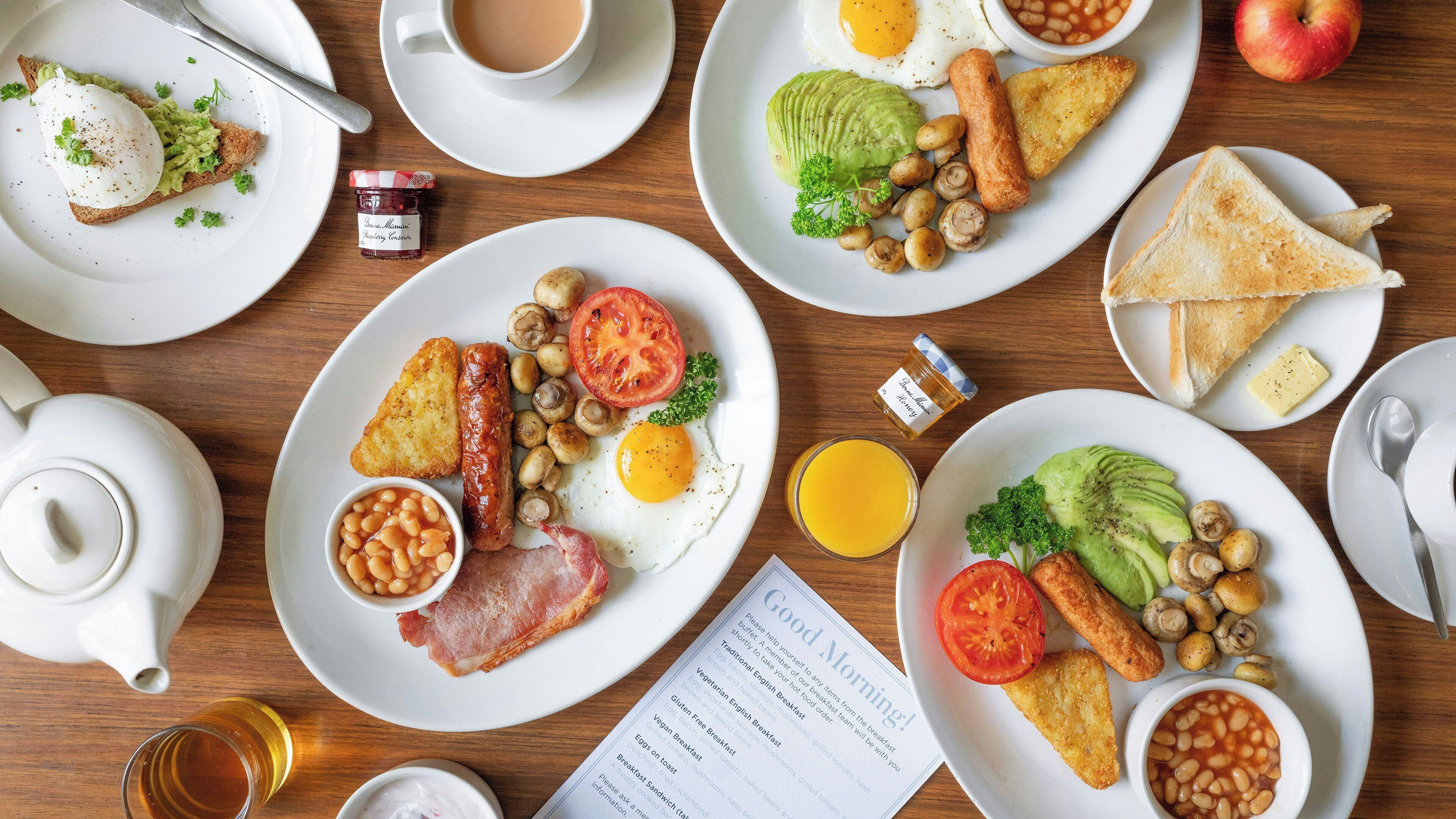 Un assortiment de plats pour le petit-déjeuner, avec une théière, est disposé sur une table en bois.