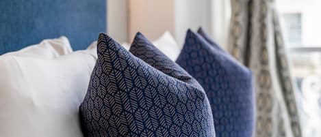 Una cama con almohadones estampados y una lámpara fijada a la pared.