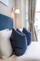Una cama con almohadones estampados y una lámpara fijada a la pared.