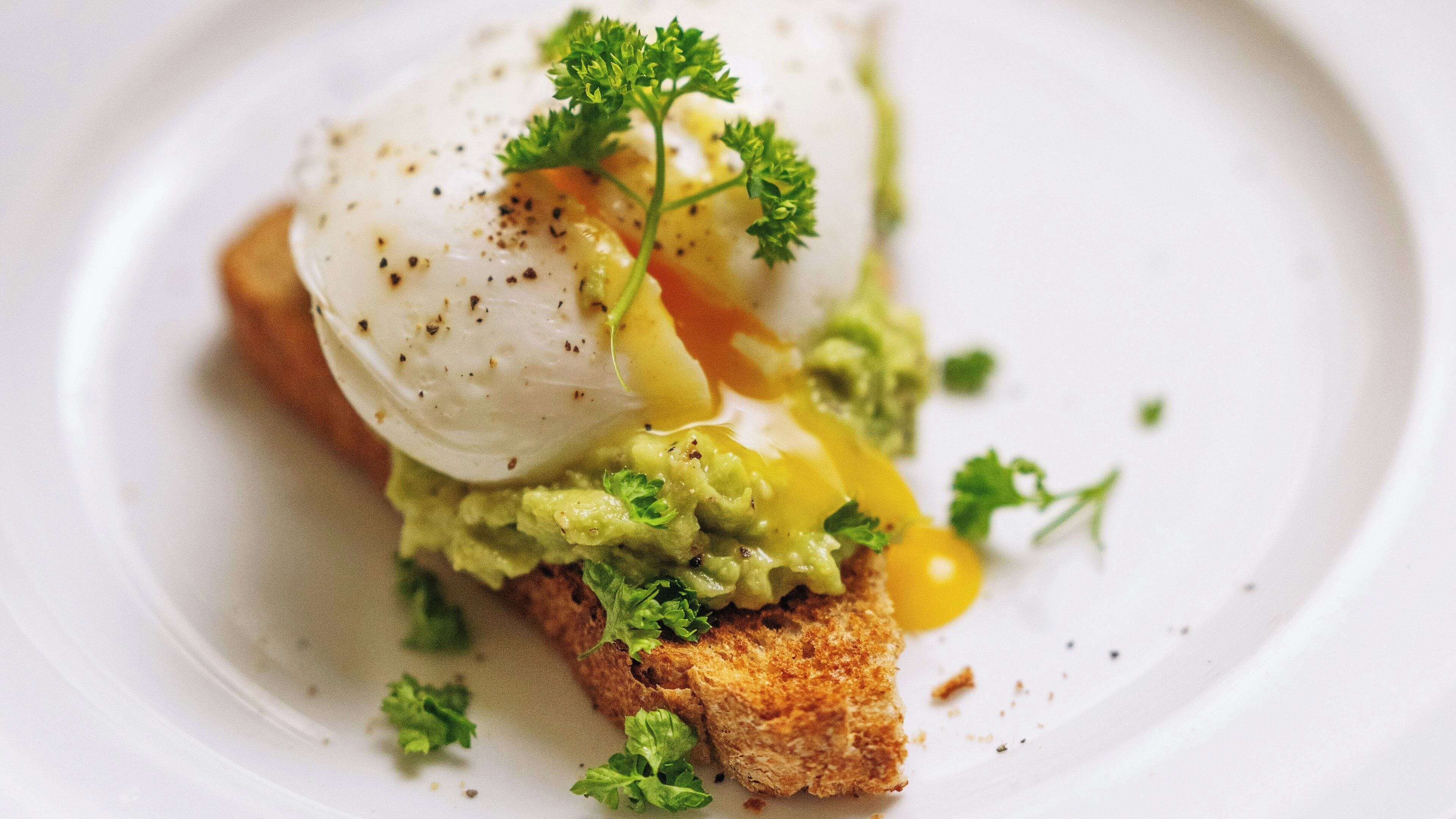 A dish with poached egg, avocado, and greens on toast.