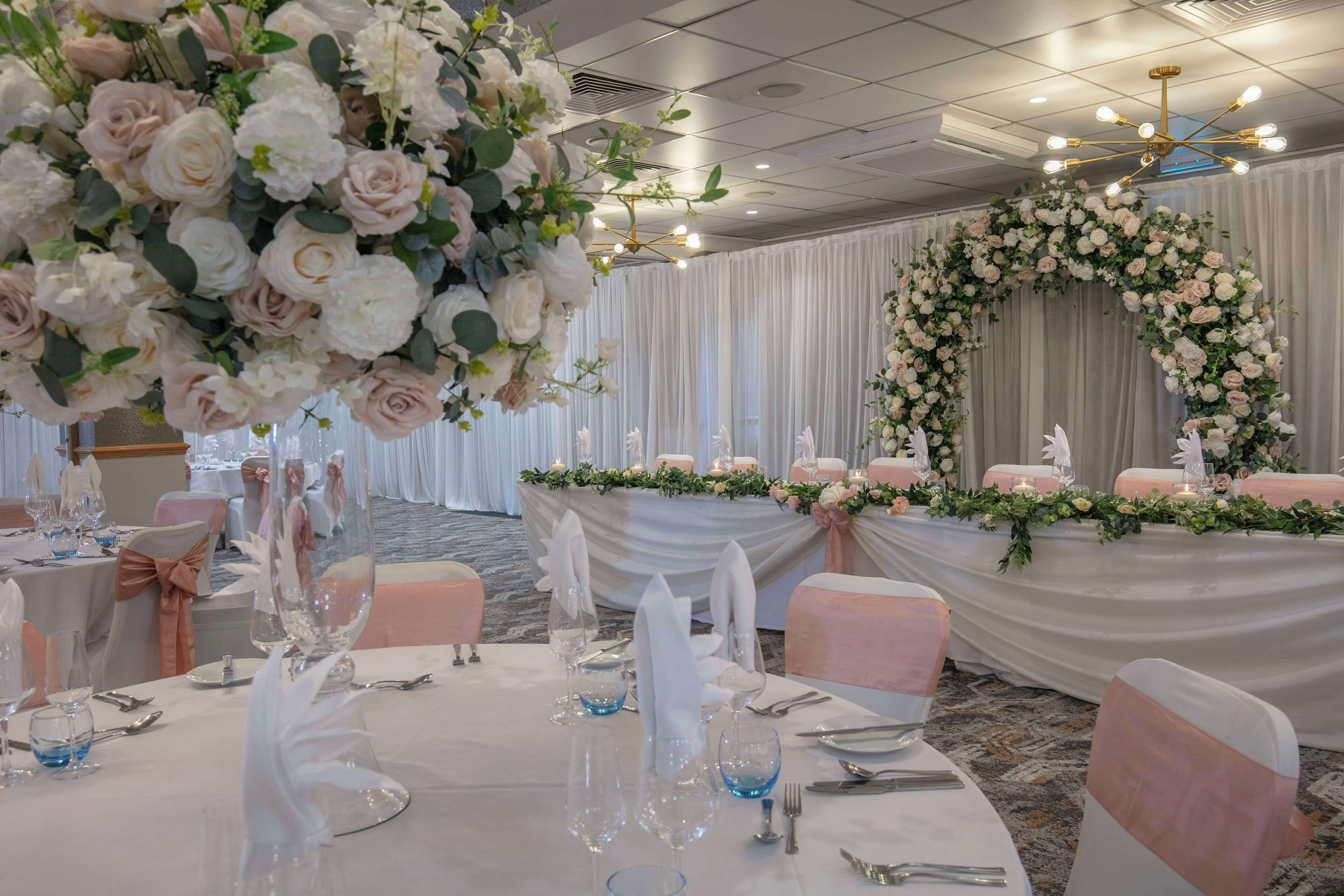 A banquet hall with round tables set for a formal event, adorned with floral centerpieces and elegant table settings.