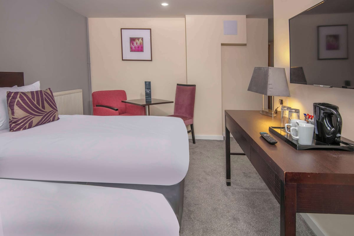 Une chambre d’hôtel avec deux lits, un bureau avec une lampe, une chaise, une machine à café et une télécommande.