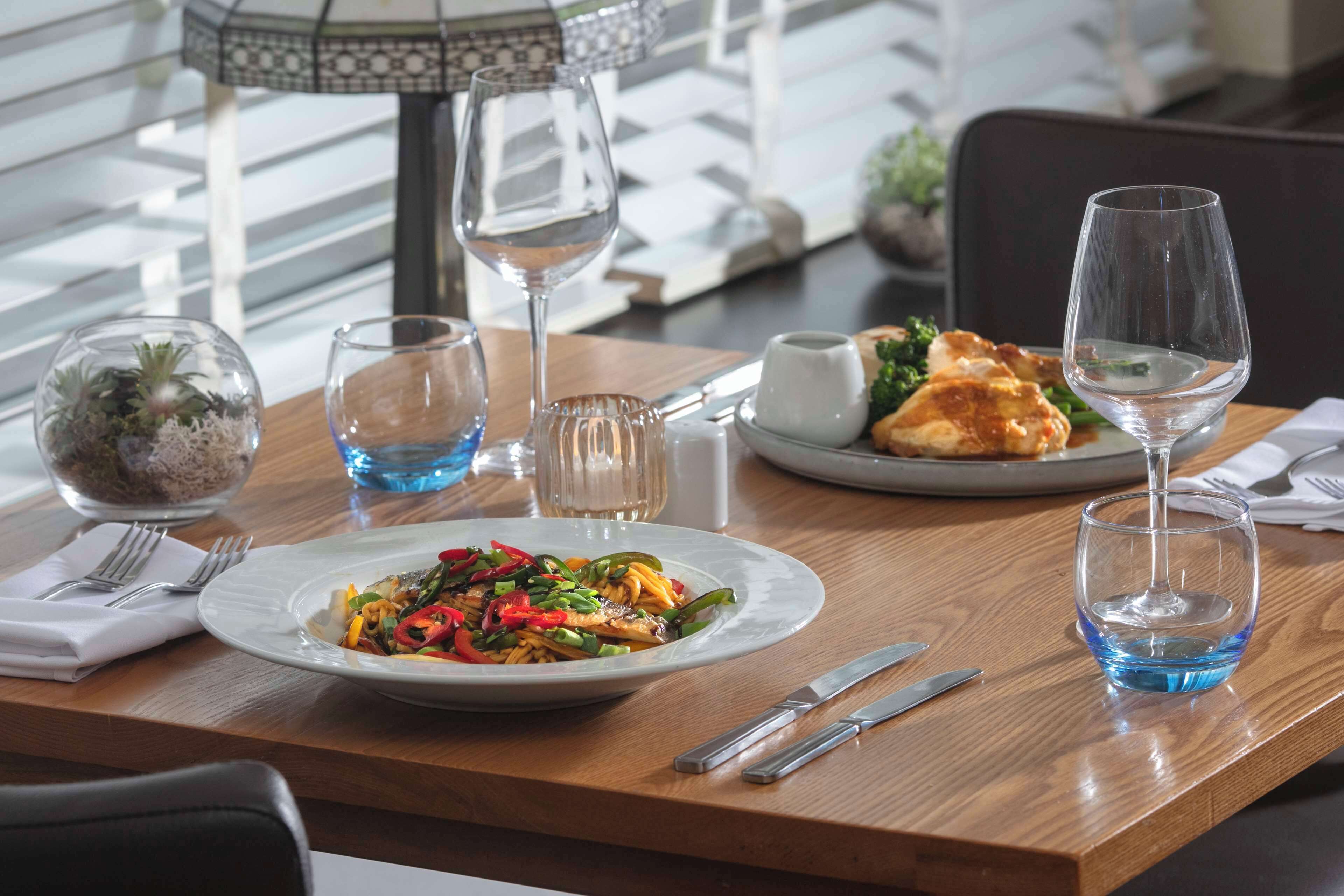 Una mesa de comedor con platos de comida, copas de vino y cubiertos.