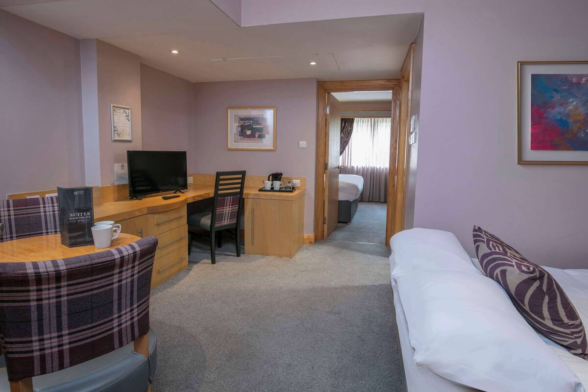 Une chambre d’hôtel avec un lit, un bureau avec un ordinateur, une chaise, un canapé et une petite table avec une tasse à café.