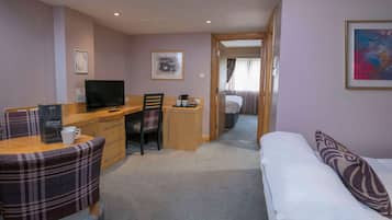 Una habitación de hotel con una cama, un escritorio con computadora, una silla, un sofá y una mesita con una taza de café.