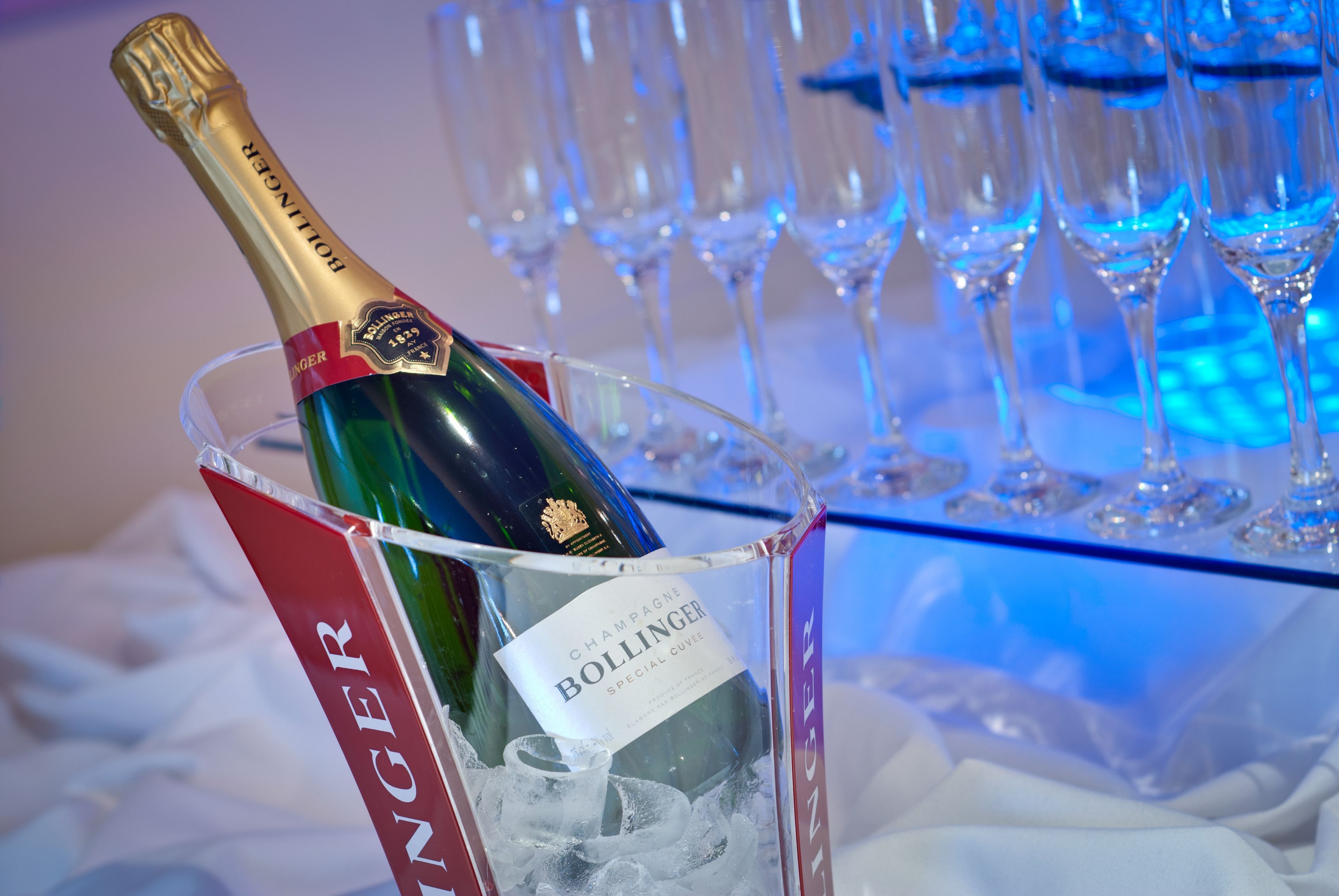 A bottle of Bollinger champagne in a glass container with ice cubes, surrounded by empty champagne flutes.