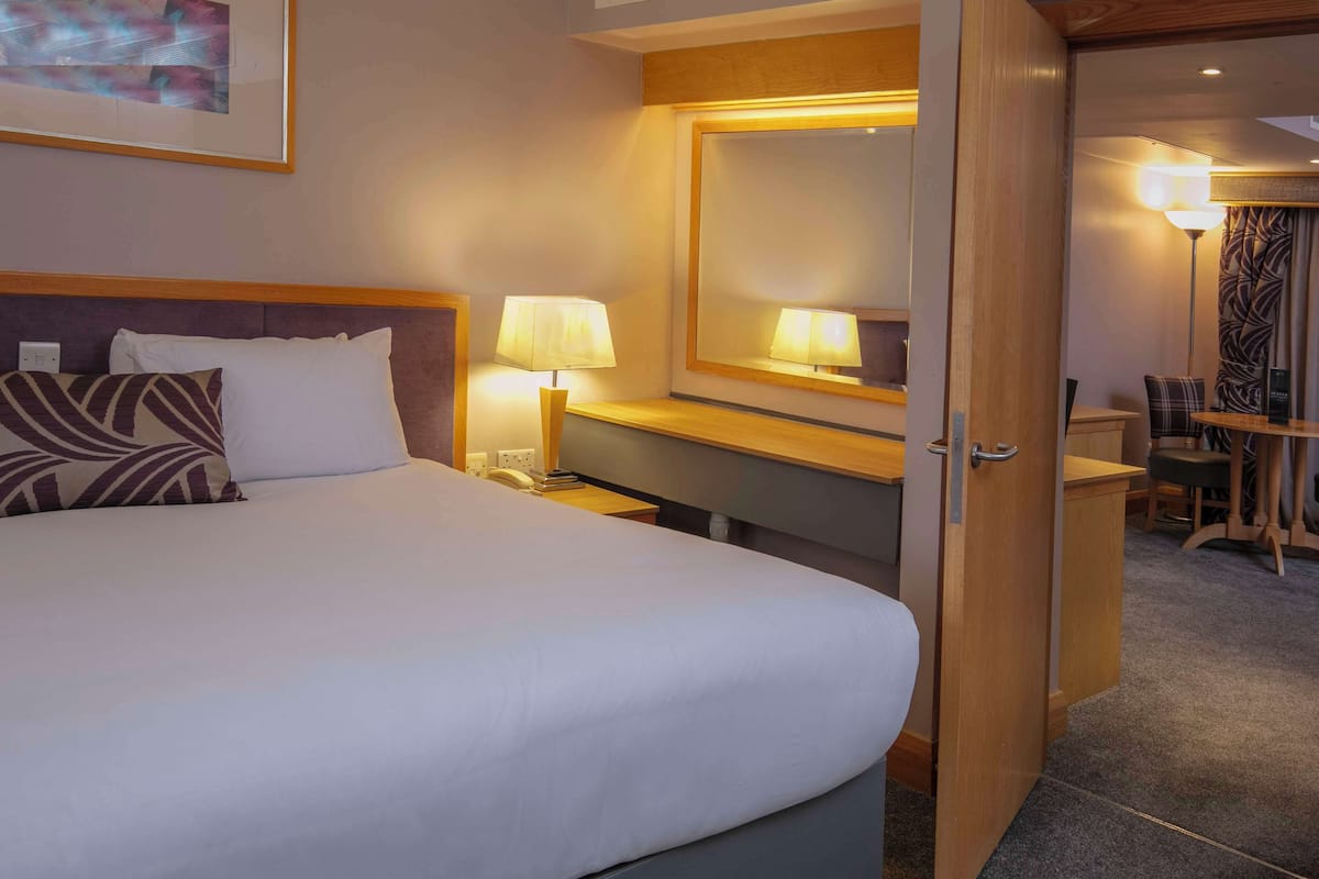 Une chambre d’hôtel avec un lit bien fait, des lampes de chevet, un bureau en bois et un miroir.