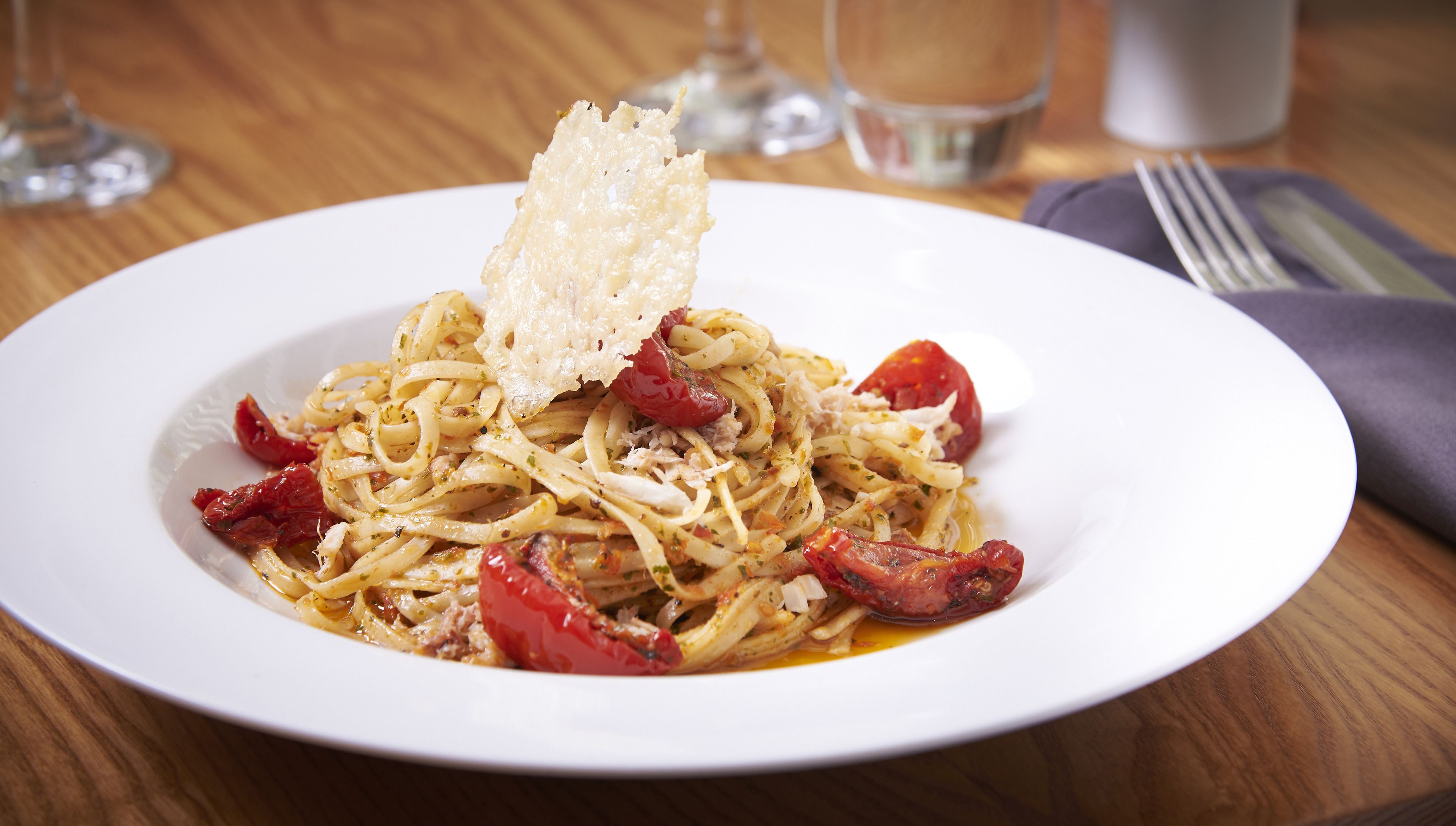 Un plato de pasta con tomates cherry y queso rallado sobre un plato blanco.