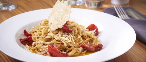 A plate of pasta with cherry tomatoes and shaved cheese on a white plate.