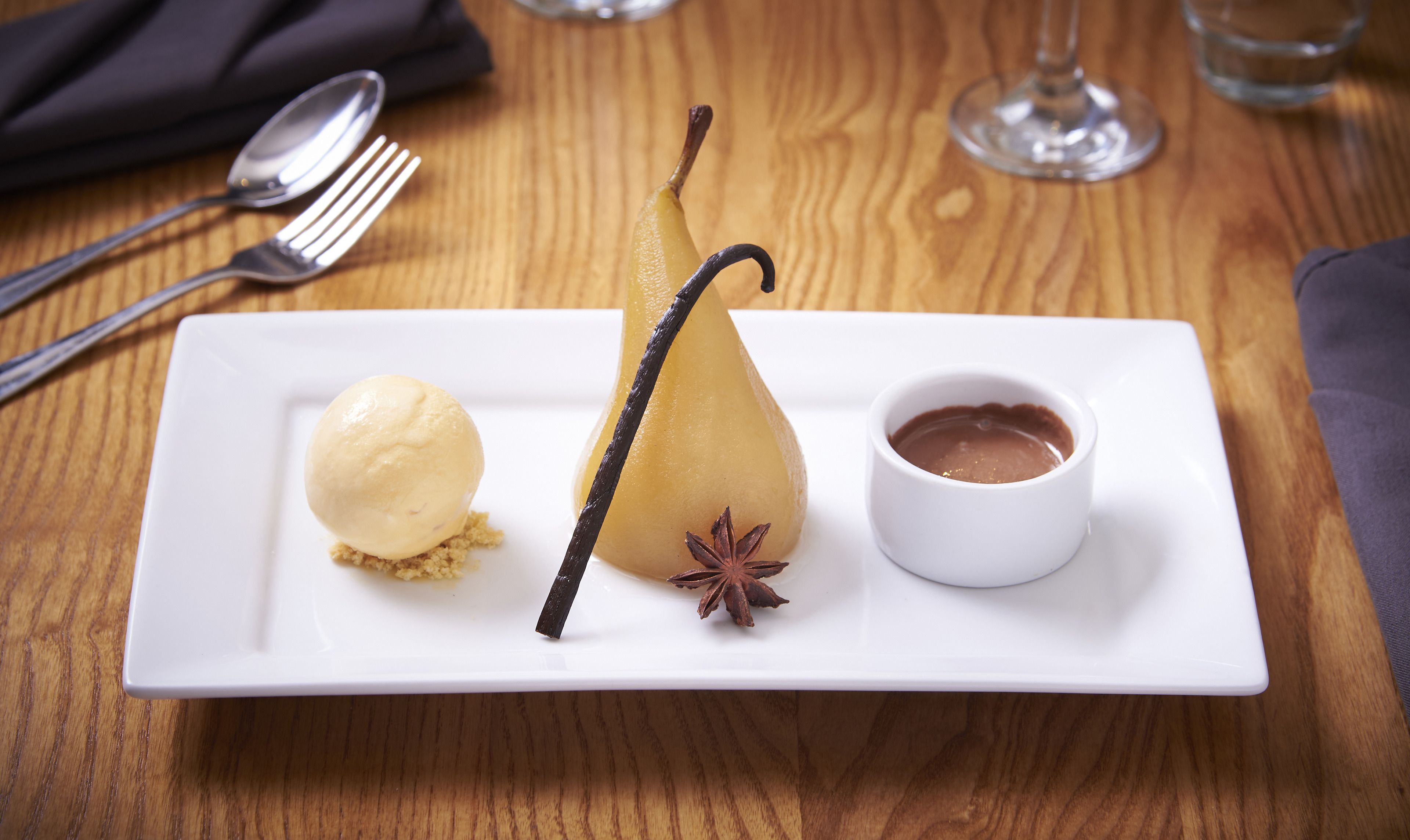 Un piatto dessert con una pera, una bacca di vaniglia, anice stellato e salsa al cioccolato.