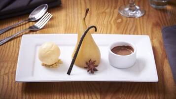 A dessert plate with a pear, vanilla pod, star anise, and chocolate sauce.