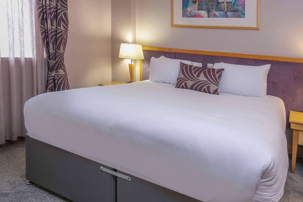 Une chambre d’hôtel avec un grand lit, une table de chevet avec une lampe et un tableau au mur.