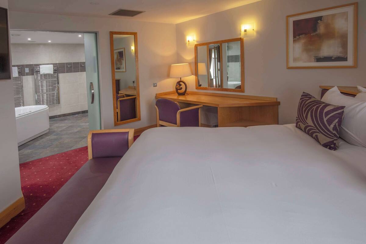 Une chambre d’hôtel avec un grand lit, un bureau avec une chaise, un miroir et un tableau au mur.