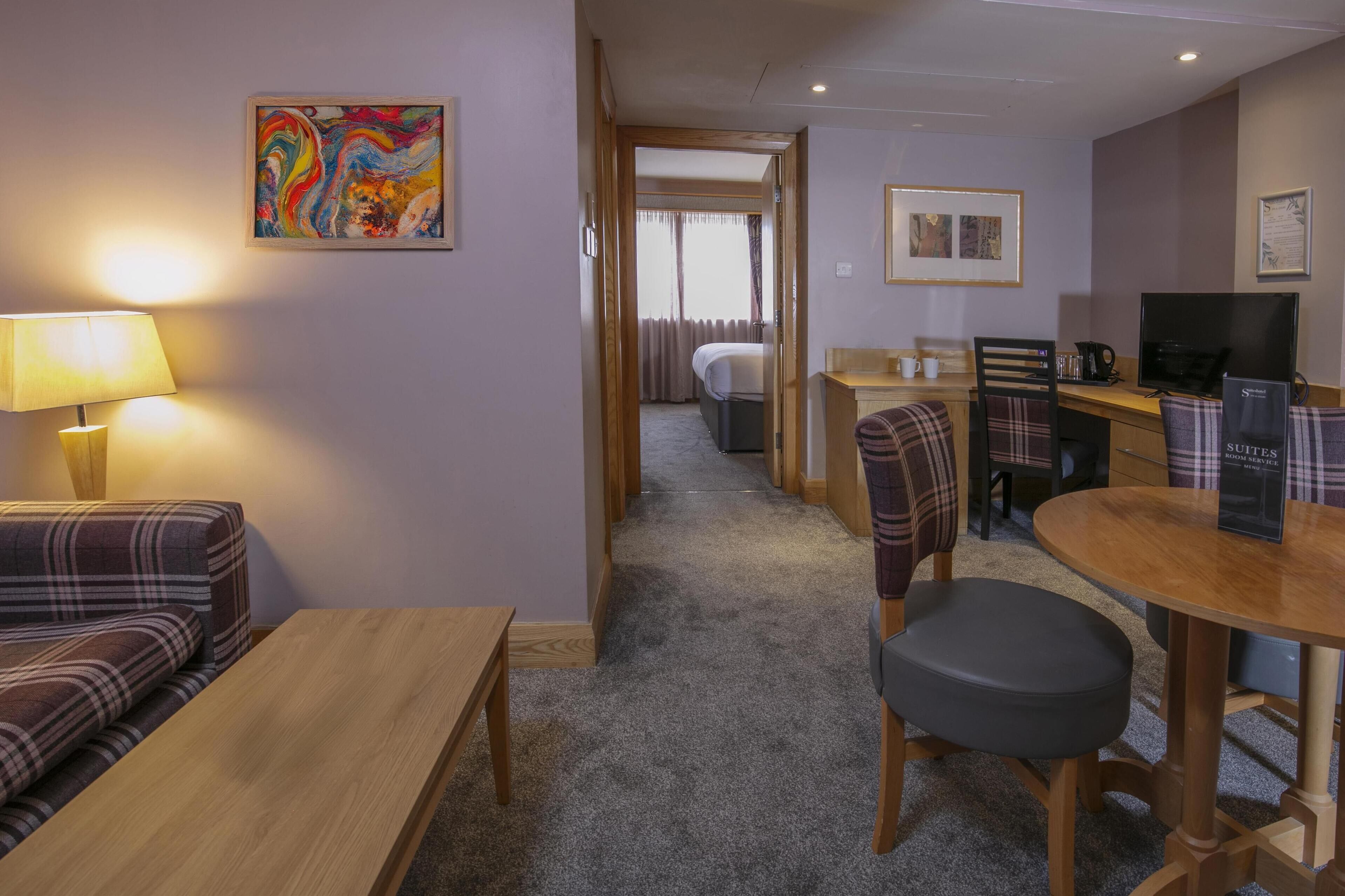 Ett hotellrum med en soffa, ett matbord, en tv och en tavla på väggen.