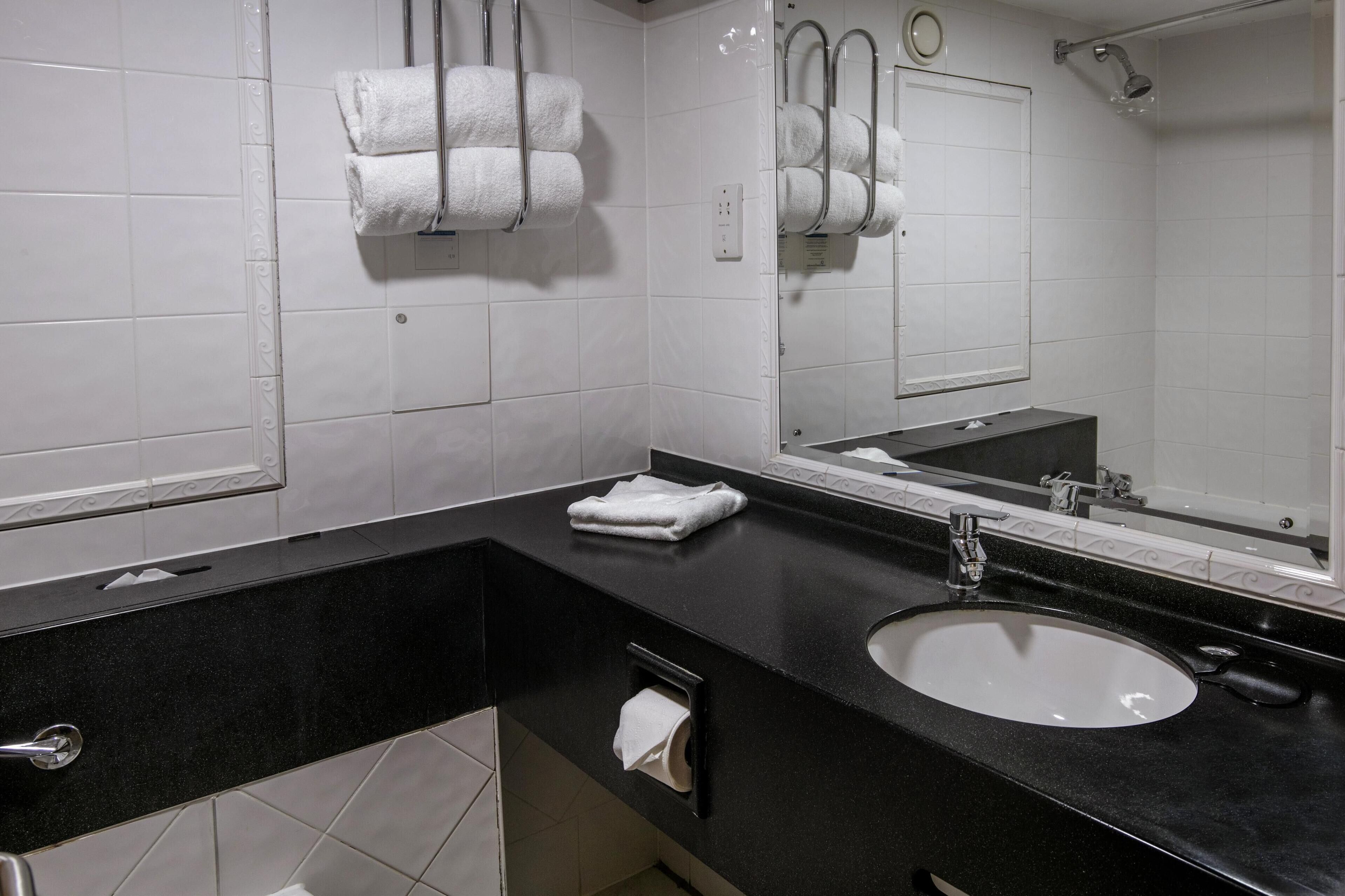 A modern bathroom with a black countertop, white sink, and two towel racks with white towels.