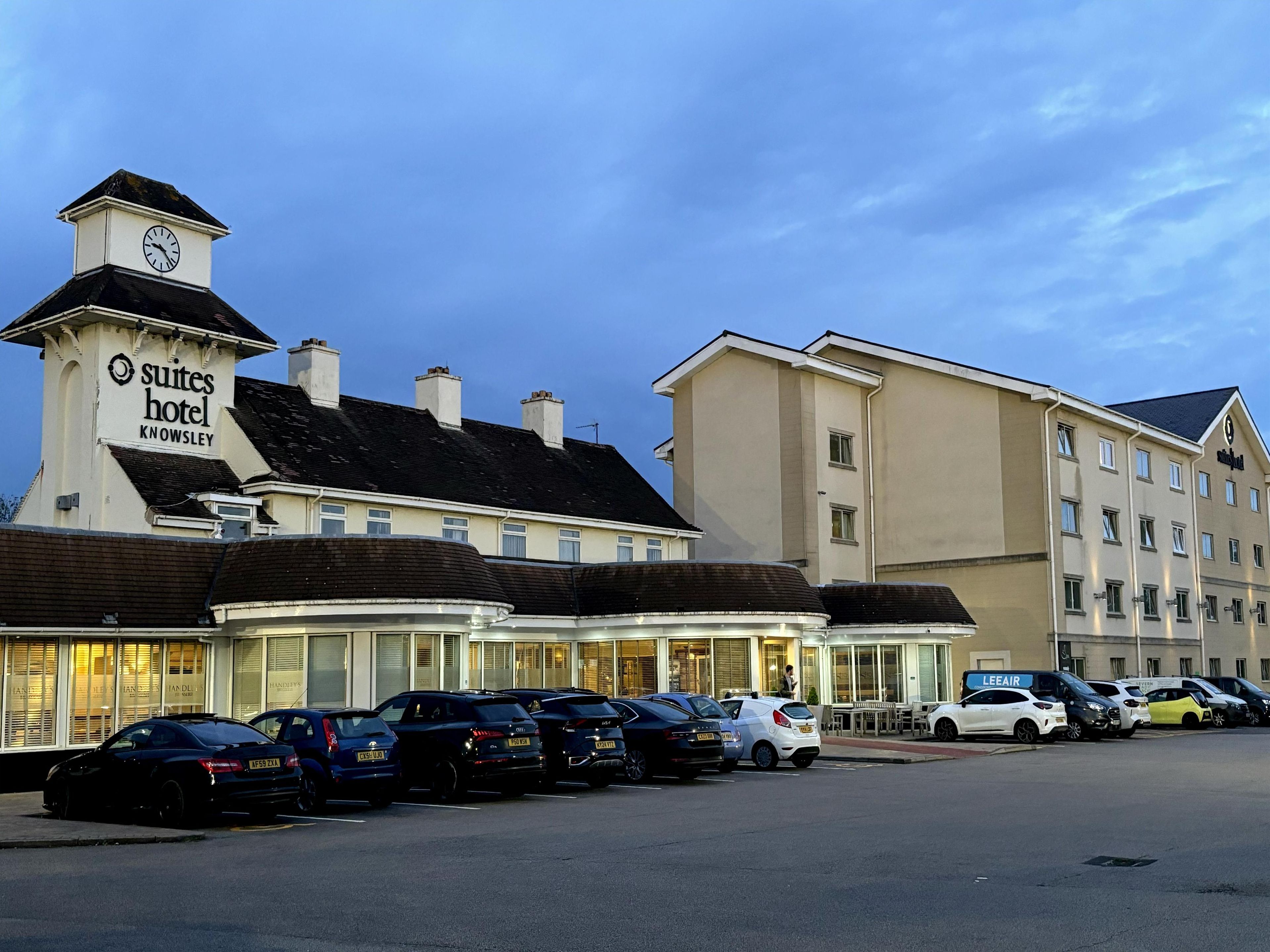 Un hotel con una torre de reloj, varios espacios de estacionamiento y un edificio moderno con un letrero que dice "LEE AIR".
