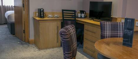 A hotel room with a bed, a desk with a computer, a coffee maker, and a sign for the suites room service menu.