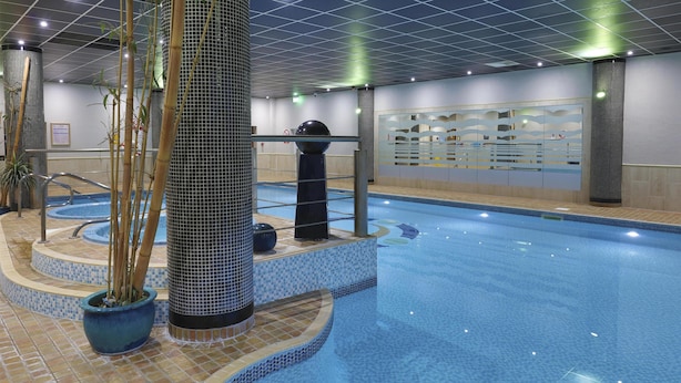 An indoor swimming pool with tiled walls, a central column, and a small waterfall feature. - Best Western Premier Suites Hotel & Spa Liverpool-Knowsley (Liverpool)