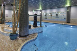 An indoor swimming pool with tiled walls, a central column, and a small waterfall feature. - Best Western Premier Suites Hotel & Spa Liverpool-Knowsley (Liverpool)