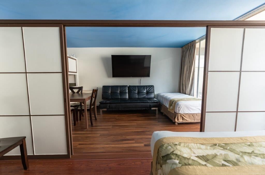 Quarto com cama, sofá, televisão fixada na parede e piso de madeira.