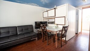 A compact living space with a sofa, dining table, chairs, a television, and a kitchenette. - Holiday Surf Hotel (Honolulu)
