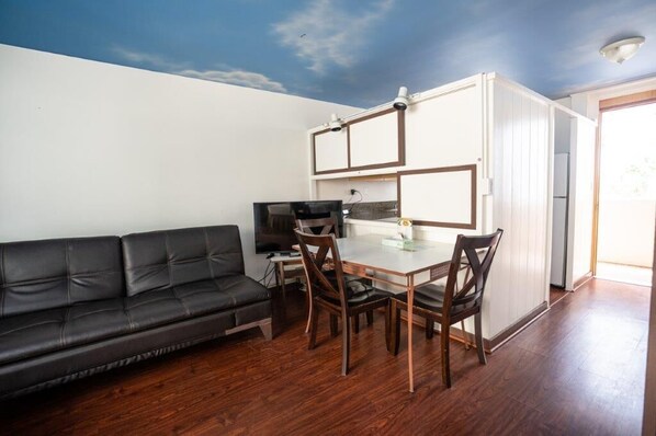 A compact living space with a sofa, dining table, chairs, a television, and a kitchenette.