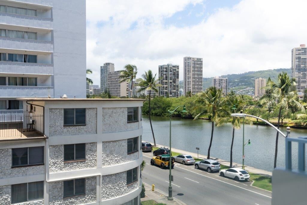 A multi-story hotel with balconies, a view of a river, and palm trees.
