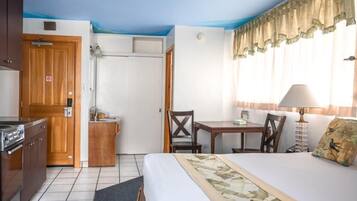 A hotel room with a bed, a desk, a chair, a small kitchenette, and a window with curtains.
