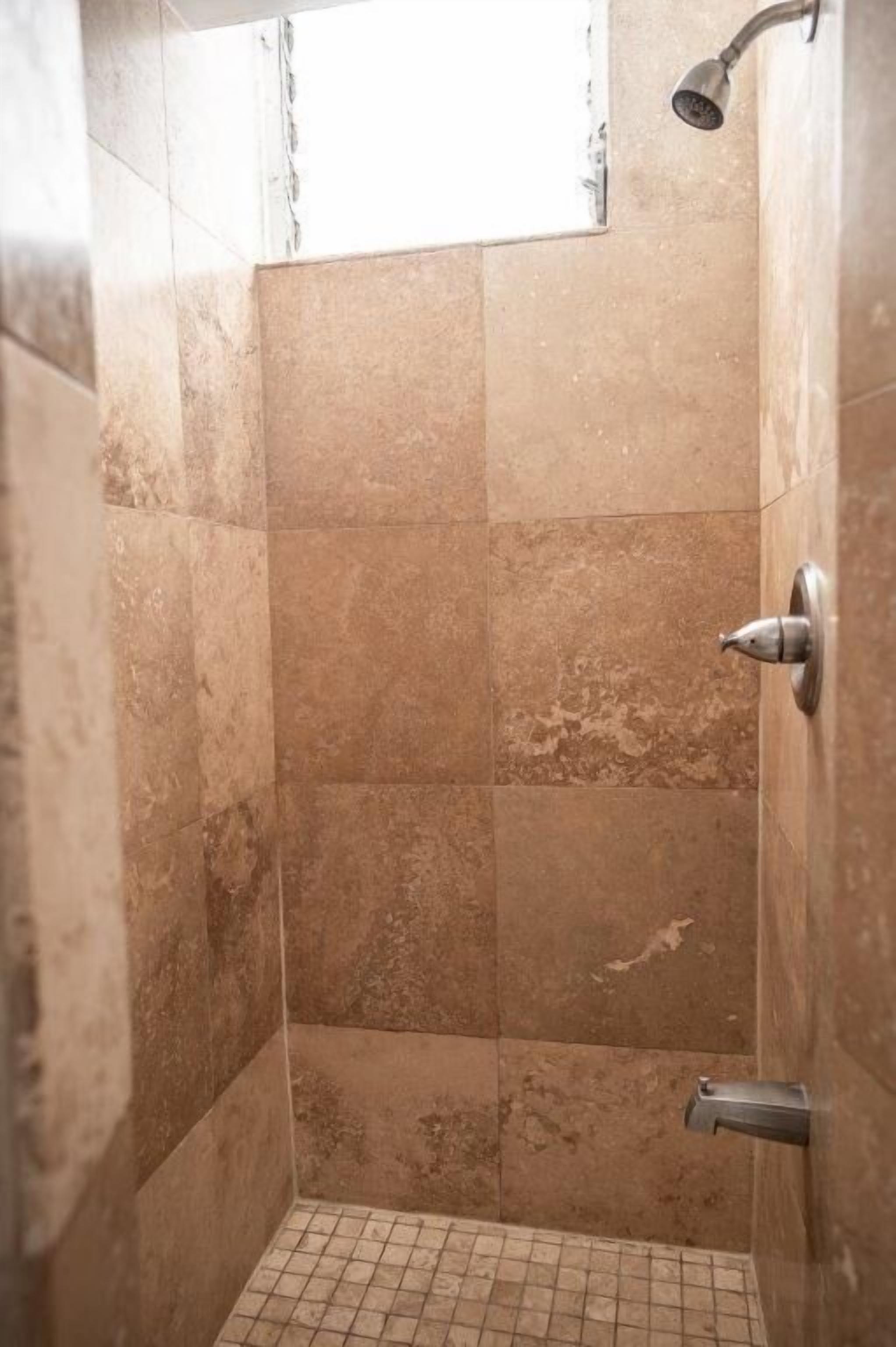 A small, tiled shower room with a showerhead and a door handle.