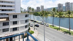 A modern building with a balcony overlooking a street with palm trees and a body of water. - Holiday Surf Hotel (Honolulu)
