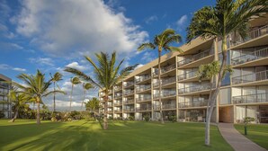 A multi-story hotel with balconies, surrounded by well-maintained lawns and palm trees. - Maui Sunset - Maui Condo & Home (Kihei)