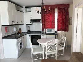 A compact kitchen with a washing machine, a microwave, and a dining area with two chairs.
