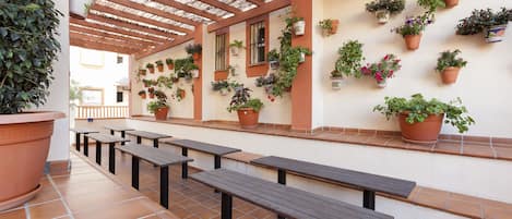 An outdoor patio with terracotta-tiled flooring, wooden benches, and a variety of potted plants on the walls.