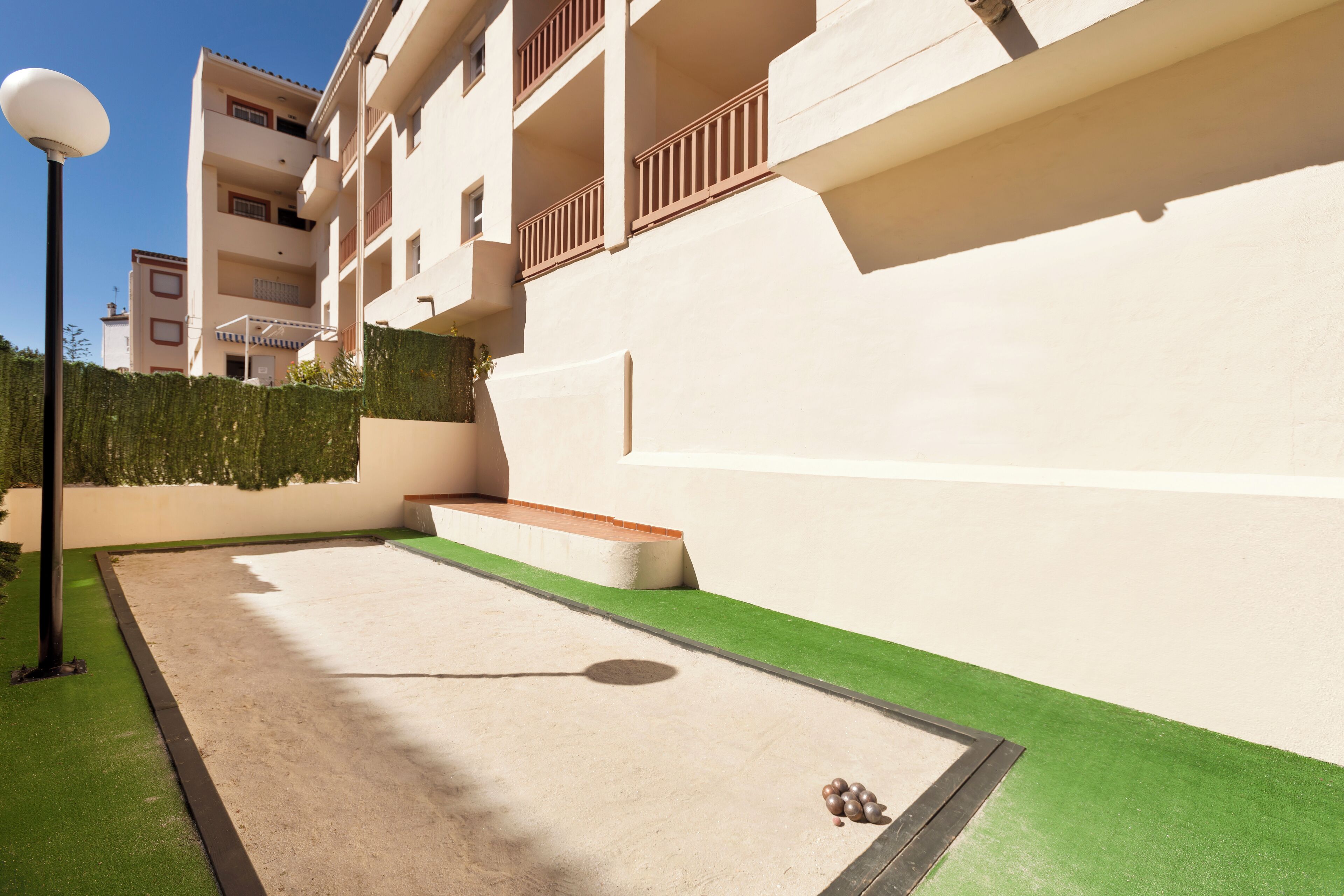 A courtyard with artificial turf, a lamp post, and a small dog.