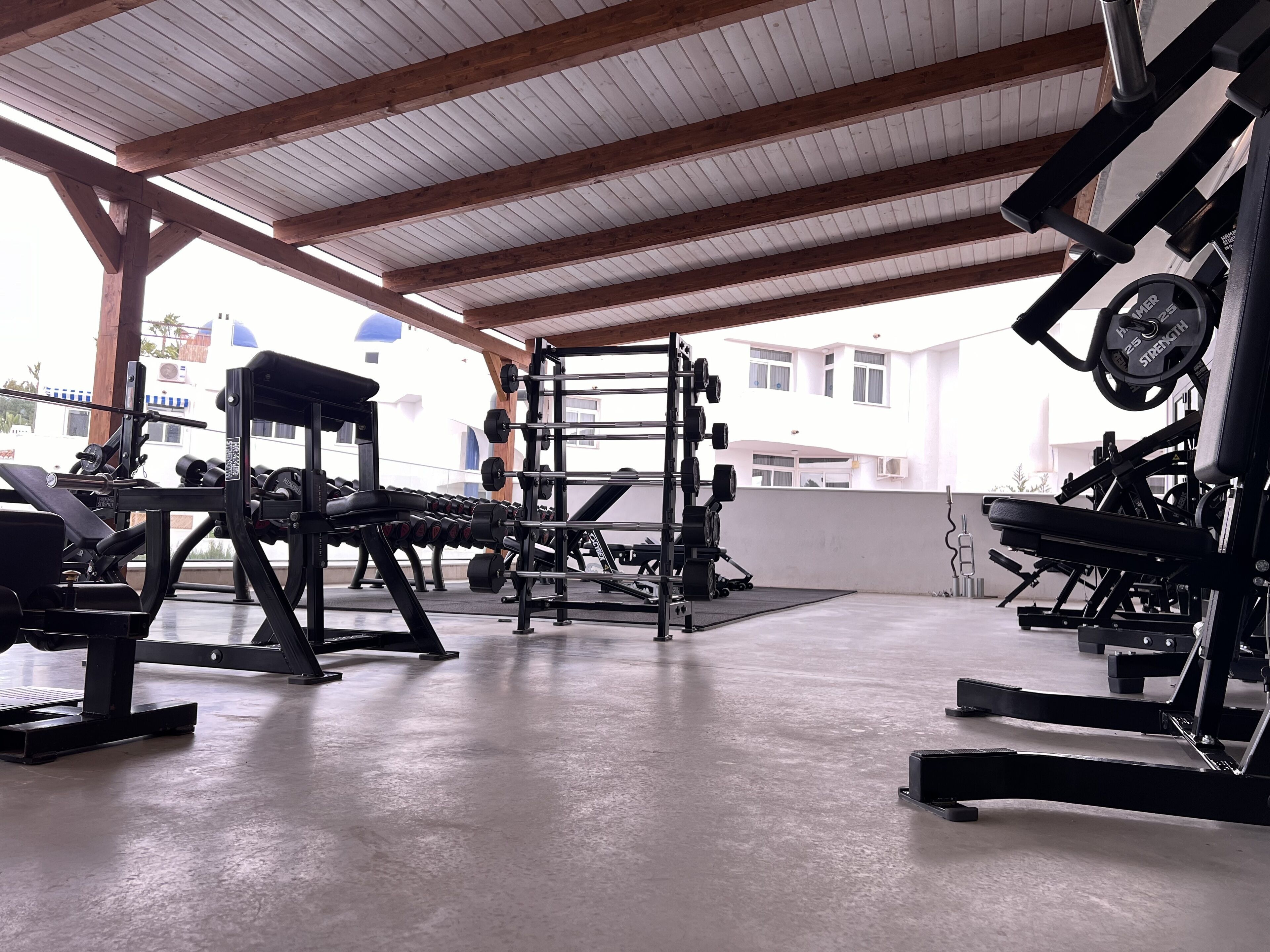 Un gimnasio con diversos equipos de ejercicio, incluyendo mancuernas, una prensa de banca y una estructura para sentadillas.