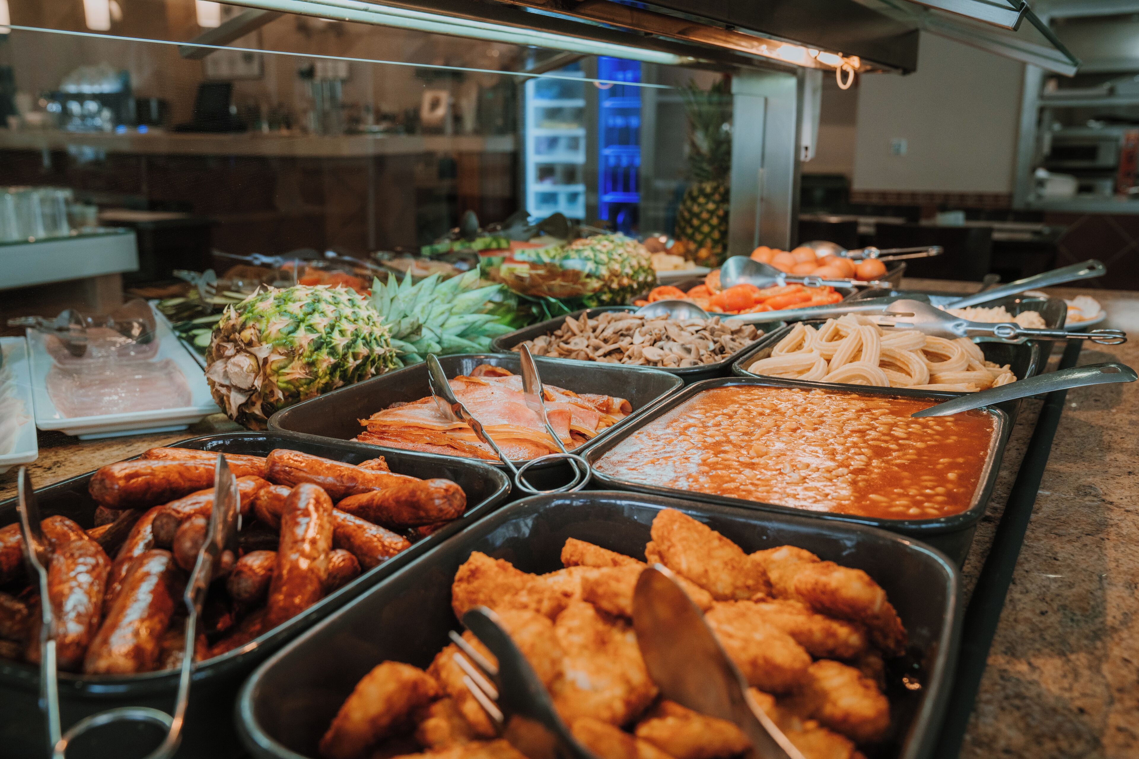 A buffet with various food options including sausages, fried chicken, and pasta.