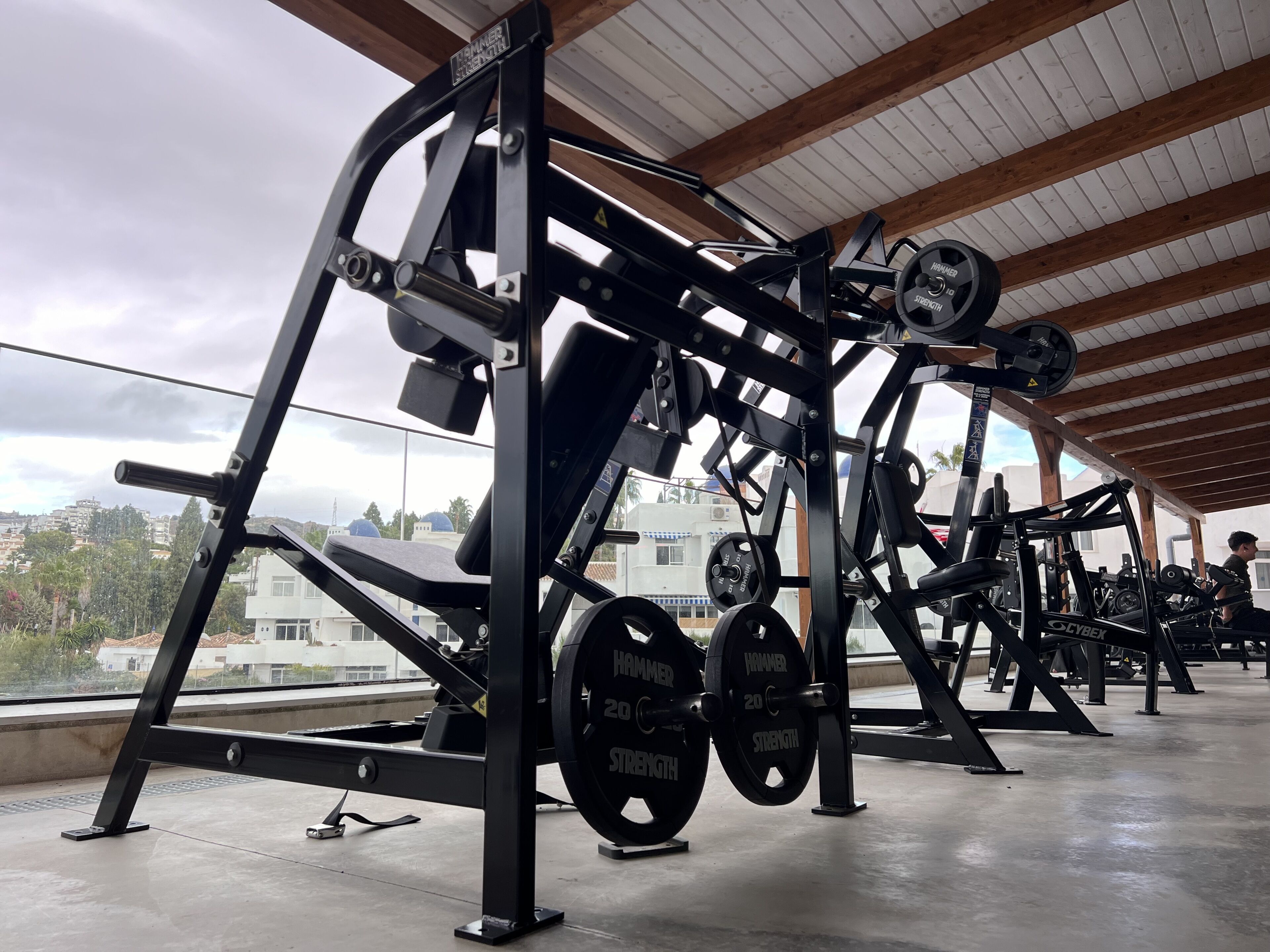 Ein Fitnessraum mit verschiedenen Gewichteinrichtungen, darunter Bänke und Kurzhanteln, unter einer Holzbalkendecke.