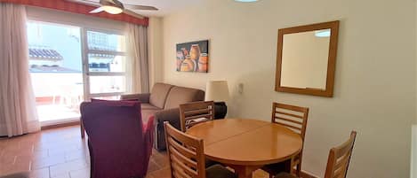 Un comedor con una mesa redonda de madera, cuatro sillas, un ventilador de techo y un gran ventanal con cortinas.