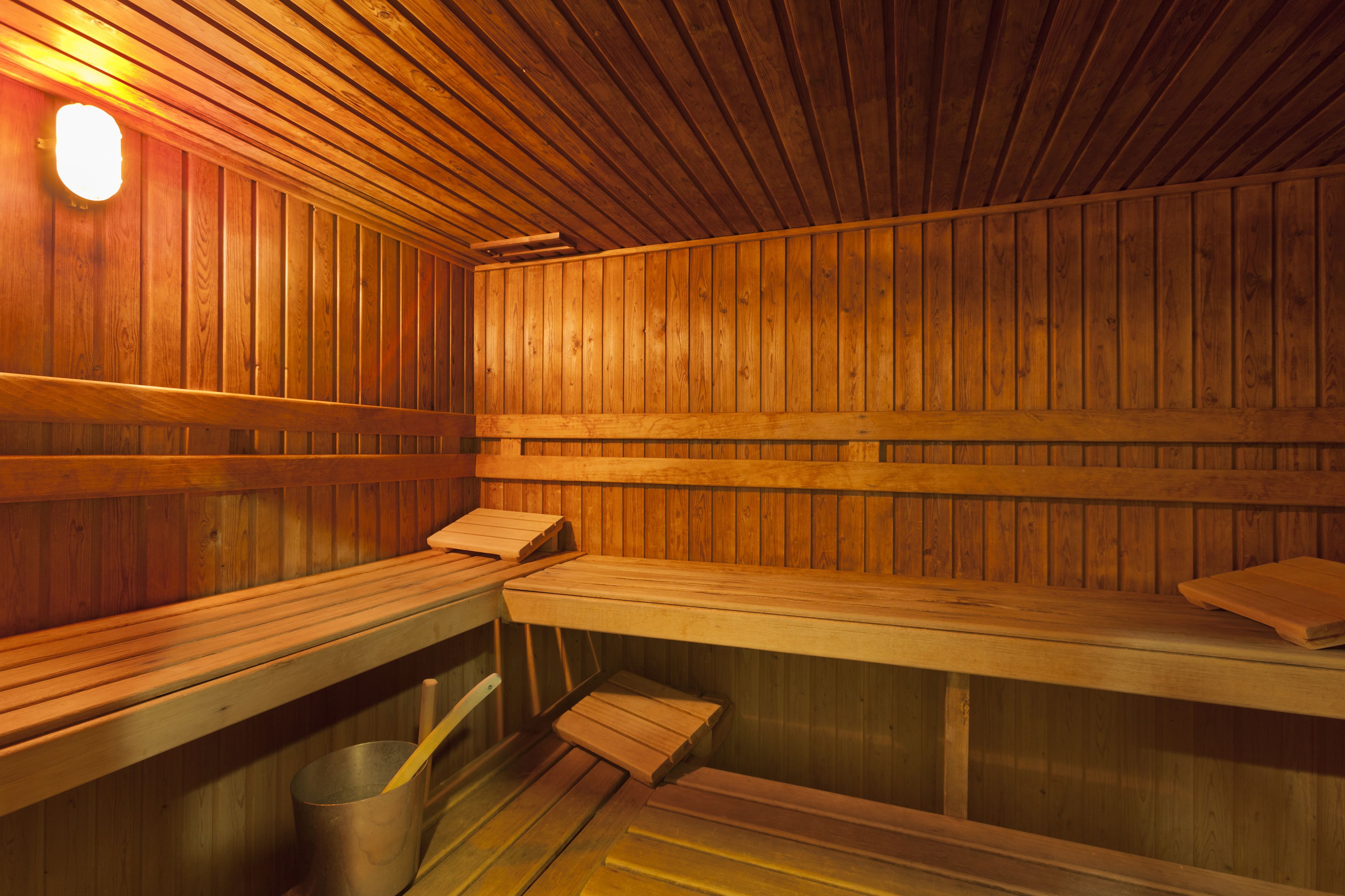 A sauna with wooden benches and a metal bucket.
