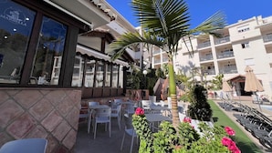 Un hotel con terraza al aire libre, palmeras y zona de piscina.
